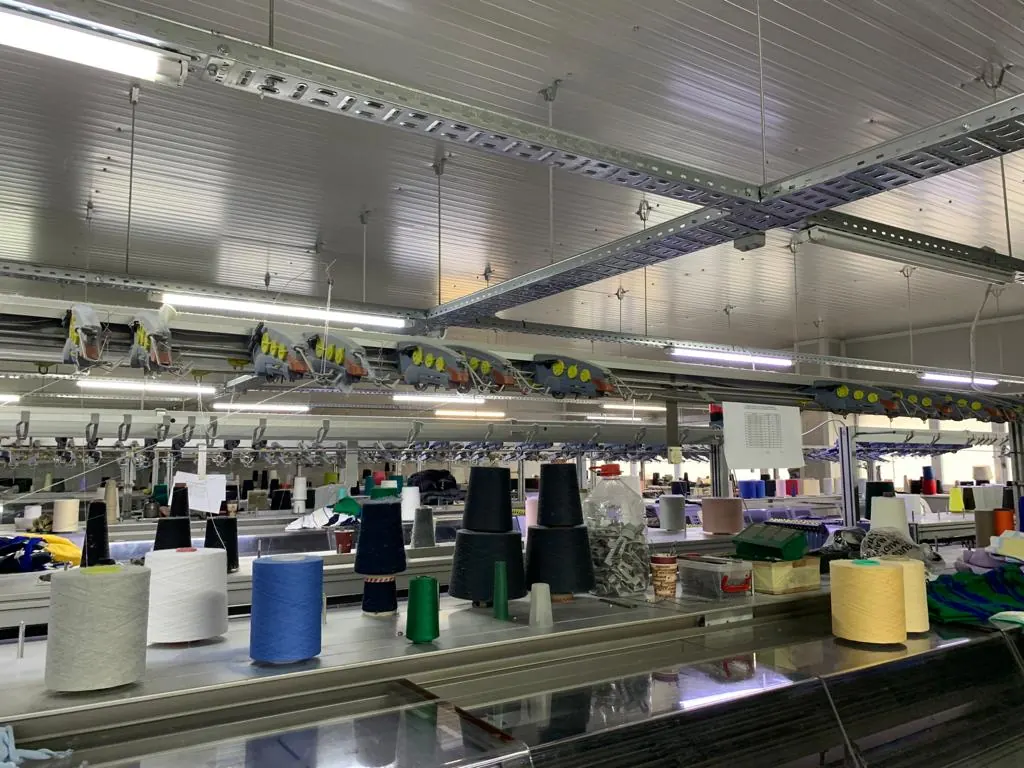 Yarn cones beside STOLL flat knitting machines